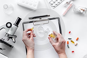 Do medcal tests. Hands hold pills near microscope on white background top view