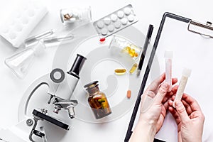 Do medcal tests. Hands hold test tube near microscope on white background top view