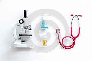 Do medical research with microscope, stethoscope, test-tubes in lab on white background top view