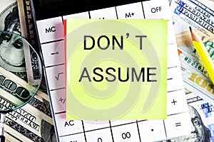 DO NOT ASSUME text, a word written on a sticker lying on a calculator against a background of money