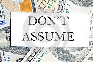 DO NOT ASSUME text, a word written on a white business card against a background of money