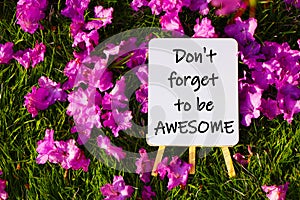 Do not forget to be awesome. On background of pink flowers and green grass.