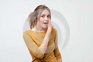 Do not tell anyone concept. Talkative teenager in yellow sweater is saying secret news looking at camera.