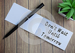 Do not wait until tomorrow text on notepad with potted plant on a wooden desk