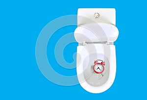 Do not waste your time advice.  Alarm clock is in the toilet bowl. Wasting time concept. Isolated on blue, copy space