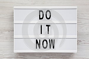 `Do it now` words on a lightbox on a white wooden background, top view. Flat lay, overhead, from above. Close-up