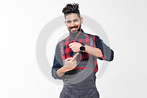 We do ontime. Young confident handyman with beard in blue overall and red t-shirt standing and showing time on his wrist watch