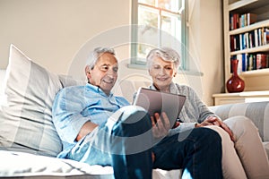 So do people still read books these days. a senior couple using a digital tablet together in their living room at home.