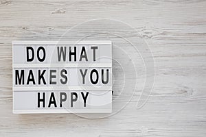 `Do what makes you happy` words on a modern board on a white wooden background, top view. Overhead, from above, flat lay. Copy