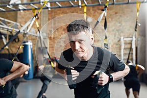 Do what you need. Athletic young man doing fitness TRX training exercises at industrial gym. Push-up, group workout