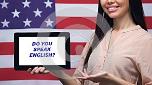 Do you speak English phrase on tablet screen in female hands USA flag background