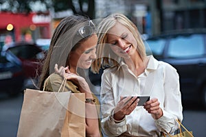 Do you think I should get one of these. A woman showing her friend something on a cellphone while theyre out shopping in