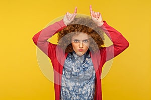 Do you want problems? Portrait of angry curly-haired woman showing bull horn gesture and threatening to attack