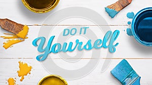 Do it yourself text on a white wooden table surrounded by color brushes, boxes and few color drops