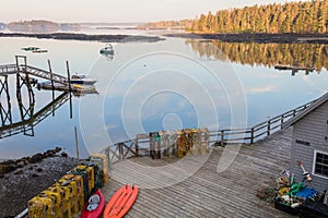 Dock and boats in bay in Boothbay, Maine, at sunrise in summer in soft beautiful light on reflective water