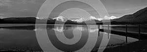 A Dock And Mountains Reflected In A Lake In Black And White