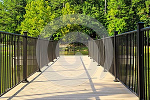 A dock over silky green lake water with a black rod iron railing surrounded by lush green trees and grass at Huddleston Pond Park