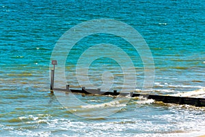 Dock pilings on a sandy beach, blue ocean and yellow sand, sunny