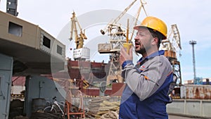 Dock worker with yellow helmet and walkie-talkie directs the cargo crane in Shipping port
