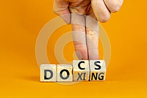 Docs or doxing symbol. Concept words Docs Doxing on wooden block. Beautiful orange table orange background. Businessman hand.