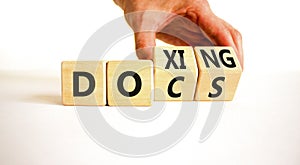 Docs or doxing symbol. Concept words Docs Doxing on wooden block. Beautiful white table white background. Businessman hand.