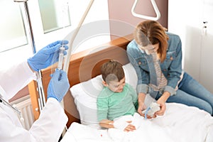 Doctor adjusting intravenous drip for little child in hospital during parent`s photo