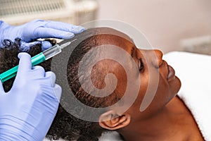 Doctor aesthetician makes head beauty injections to a female african patient