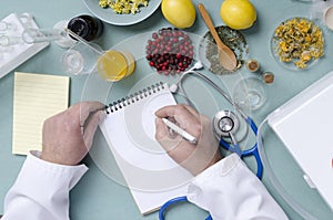 Top view of doctor`s workplace. Doctor of traditional medicine writing down the prescription for patient.Natural medicines, dry be photo