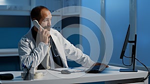 Doctor answering landline phone discussing sickness diagnosis with remote patient