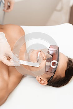 The doctor applies an epilation gel on the man`s face. The man laughs, because he is ticklish.