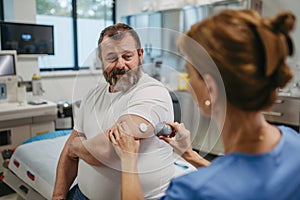 Doctor applying a continuous glucose monitor sensor on patient's arm. Obese, overweight man is at risk of developing