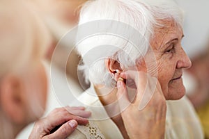 Doctor applying hearing aid to senior woman`s ear