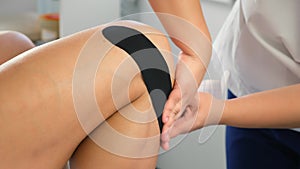 Doctor is applying kinesiology tape to woman's leg to fix the knee joint.