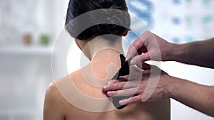 Doctor applying Y-shaped tapes on patient upper back, alternative medicine