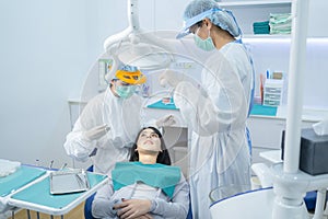 Doctor and assistance in protective masks serving Asian young woman patient by examining teeth or dental checkup at dental clinic.