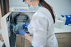 Doctor assistant in blue gloves sterilize dental steel set tools in autoclave