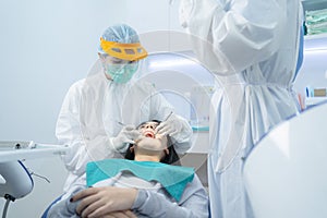 Doctor and assistant in PPE wear protective facemask due to Covid19, examining young woman patient`s teeth or dental checkup at de
