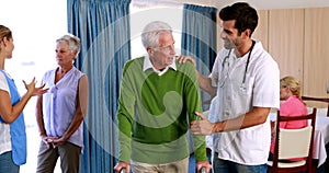 Doctor assisting seniorman to walk with walker