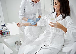 Doctor attaching intravenous drip on lady hand while she drinking water photo