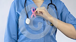 Doctor attaching pink ribbon uniform, breast anticancer campaign, women disease