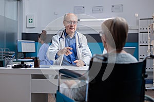 Doctor attending medical consultation with woman sitting in wheelchair at clinic