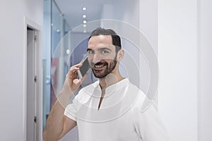 Doctor bearded young man, medical professional happy talking using a smartphone mobile phone at hospital