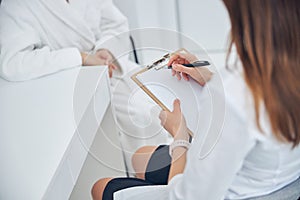 Doctor of beauty clinic writing something notes while sitting on the chair