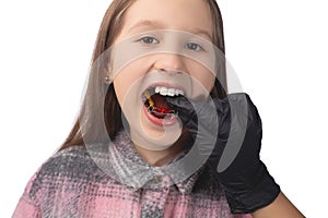 A doctor in black medical gloves tries on an orthodontic appliance for a little girl. The concept of teeth alignment in childhood