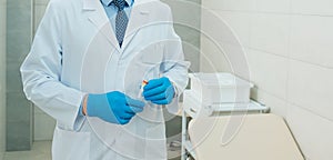 A doctor in blue gloves is holding an empty tube for testing.