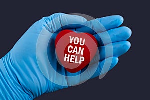Doctor in blue gloves holds a heart with text YOU CAN HELP, concept