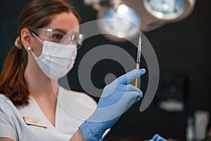 Doctor in blue glowes is standing and holding equipment. In the stomatological cabinet