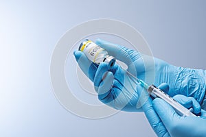 Doctor in blue latex gloves fill in syringe with vaccine from glass vial.