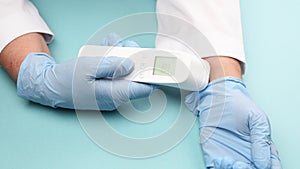 Doctor in blue latex gloves measures body temperature on the wrist with a non-contact thermometer