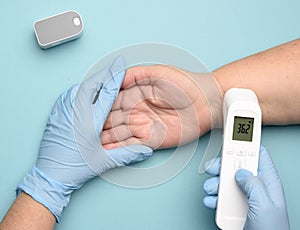 Doctor in blue latex gloves measures the temperature with an electronic contactless gadget